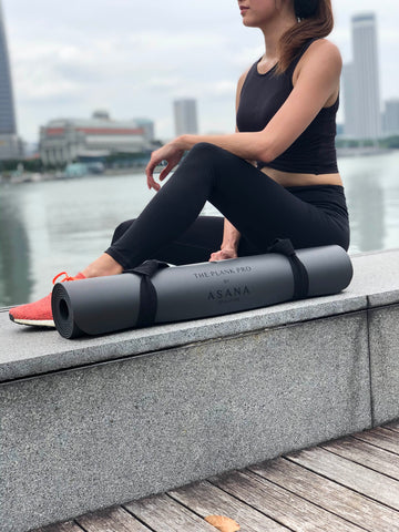 Woman in a black athleisure wear is posing next to The Plank Pro Ultimate Workout Mat by Asana Singapore